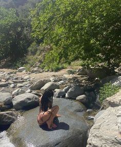 a woman sitting on top of a large rock next to a river filled with water