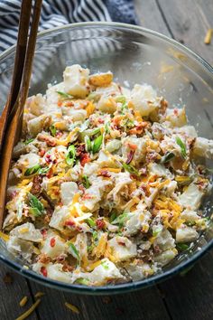 a glass bowl filled with potato salad next to two wooden spoons on top of a table