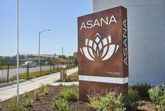 a sign for asana next to a road with cars on the street in the background