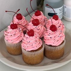 cupcakes with pink frosting and cherries are on a plate next to a bottle of water