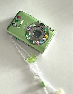 a green digital camera sitting on top of a white table next to a beaded necklace