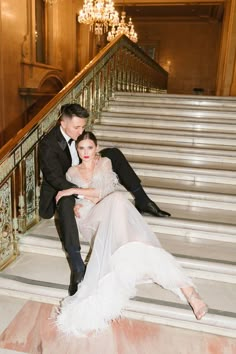 a bride and groom sitting on the stairs at their wedding reception in an ornate building