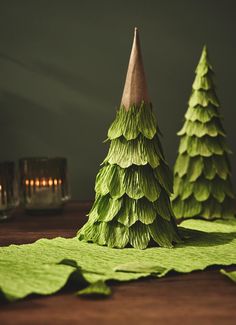 two green paper christmas trees sitting on top of a wooden table next to each other