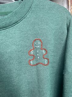 a green sweater with an orange teddy bear embroidered on it