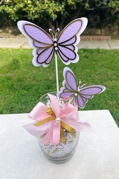 a vase filled with pink and purple butterflies on top of a white table in the grass