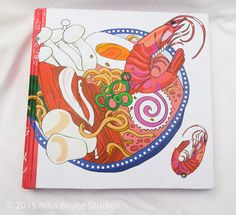 a book with an image of lobsters and noodles on it, sitting on a white sheet