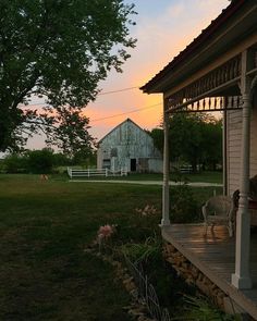 the sun is setting over an old farm house and lawn with rocking chairs on it