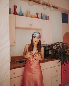 a woman standing in a kitchen with her hands on her chest and wearing a headband