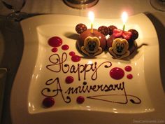 two mickey mouse candles sitting on top of a white plate with happy anniversary written on it