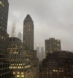 the city skyline is lit up at night, with buildings in the foreground and foggy skies