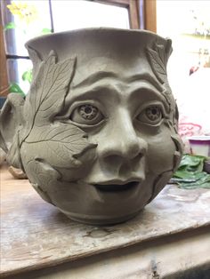 a clay pot that has a face on it's head and leaves painted on the side