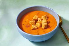 a bowl of soup with tofu cubes in it and a wooden spoon on the side