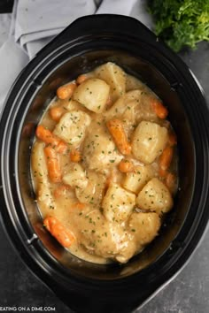 a crock pot filled with potatoes and carrots next to some parsley on the side