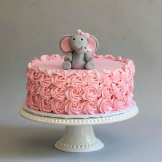 a cake with pink frosting and a small elephant on top is sitting on a pedestal