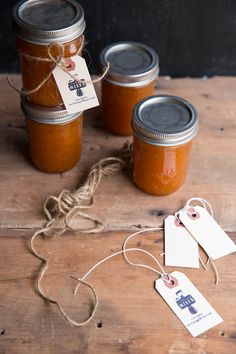 three jars filled with jam sitting on top of a wooden table next to two tags