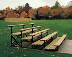 there are many benches in the park on this grassy field with autumn trees behind them