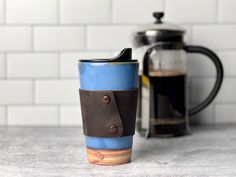 a blue and brown coffee cup sitting on top of a counter next to a metal pot