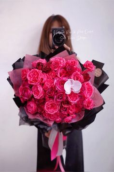 a woman holding a bouquet of pink roses in front of her face with a camera