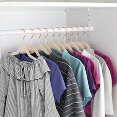 several shirts hanging on a rack in front of a white wall and some hangers