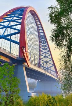 a bridge that is over some water with trees in the foreground and blue sky above it