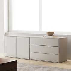 a white cabinet with two drawers and a bowl on top in front of a window