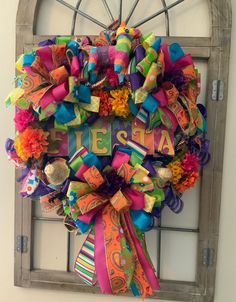 a colorful wreath is hanging on the wall next to an old window with letters and ribbons