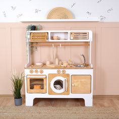 an old fashioned wooden play kitchen with pots and pans on the top shelf, next to a potted plant