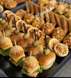 sandwiches and appetizers are arranged on a black platter with toothpicks