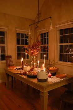 a table with candles and pumpkins on it in front of two windows at night