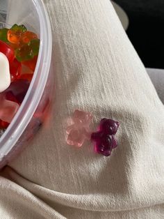 a plastic container filled with gummy bears sitting on top of a white cloth covered bed