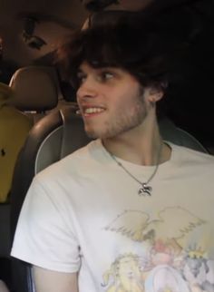 a man sitting in the back seat of a car talking on his cell phone while wearing a tshirt