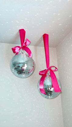 two disco ball ornaments with pink ribbons hanging from the ceiling in a room that has white walls and polka dots