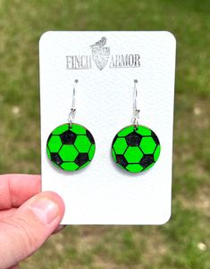 a pair of earrings with green and black designs on them, sitting in front of a white card