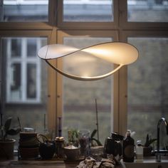 a light hanging over a kitchen counter top next to a window with lots of clutter on it