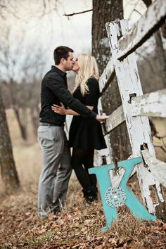 a couple kissing in front of an old wooden sign