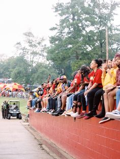 a group of people sitting on top of a red wall next to each other at a baseball game