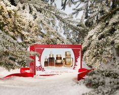 a red box with three bottles in it on top of snow covered ground next to trees