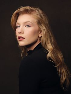 a woman with long blonde hair wearing a black sweater and gold hoop earrings, posing for a studio portrait