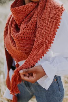 a woman wearing an orange knitted shawl and white shirt with her hands on her hips