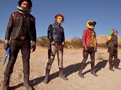 four people in helmets and bodysuits standing next to each other on the desert