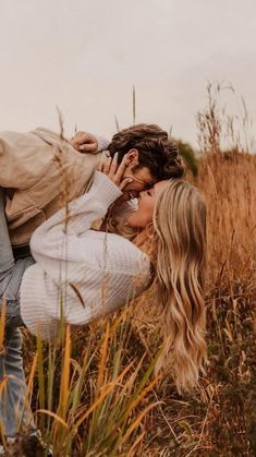 a man and woman are kissing in the middle of some tall grass with their heads close to each other