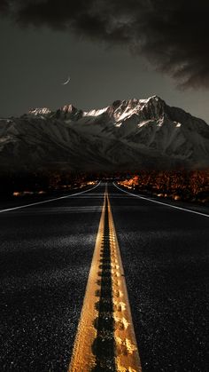 an empty road in the middle of nowhere with mountains in the background and dark clouds