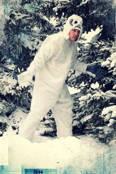 a man in a white bear suit standing next to snow covered trees and looking at the camera