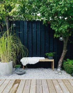 a wooden deck with potted plants and a bench in the middle, next to a black fence