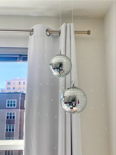 three disco ball lights hanging from a curtain in front of a window with buildings outside