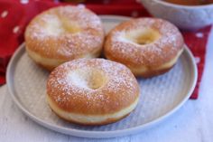 three doughnuts on a plate next to a bowl of dipping sauce