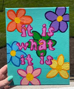 someone is holding up a painted canvas with flowers on it that says, it is what it is