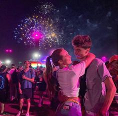 two people standing next to each other with fireworks in the sky behind them and onlookers watching