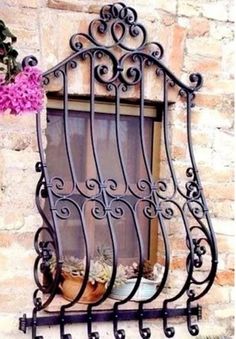 an iron window with potted plants and flowers on the ledge below it, in front of a stone wall