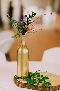 a vase with flowers in it sitting on top of a wooden slice at a table